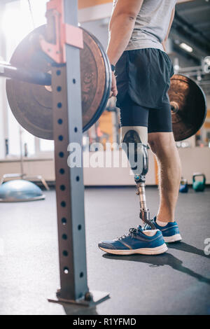 cropped shot of man with artificial leg working out with barbell at gym