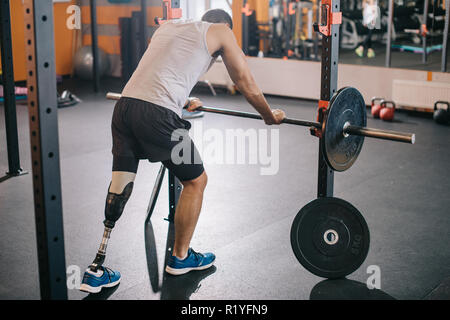 handsome young sportsman with artificial leg leaning on barbell at gym Stock Photo