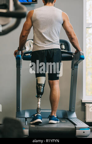 rear view of young sportsman with artificial leg walking on treadmill at gym Stock Photo