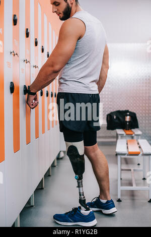 handsome young sportsman with artificial leg opening locker with electric key on his wrist at gym changing room Stock Photo