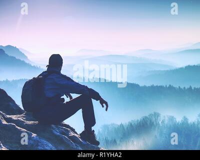 Sit on peak. The tired out tourist has reached the rocky peak of the mountain and now enjoys amazing views. Stock Photo