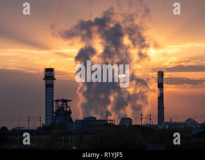 Sunrise over industrial factory with smoke rising between smokestacks. Behind smoke sun and orange clouds are visible Stock Photo