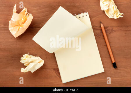 Idea Crisis. An overhead photo of a spiral note pad with a blank sheet of paper and crumpled pages, shot from above on a dark wooden background with a Stock Photo