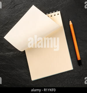 Turning a New Page. A photo of a spiral note pad with a blank sheet of paper, shot from the top on a dark background with a pencil and a place for tex Stock Photo