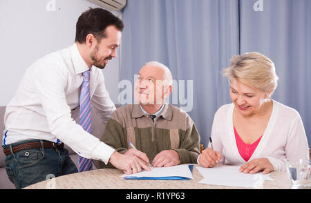 ature woman and her eldery father signing contract with smiling sales manager at home Stock Photo