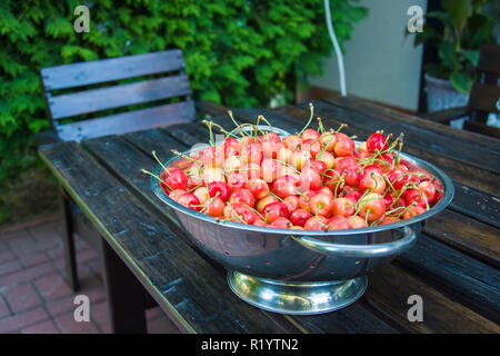 Sweet cherries in an aluminum colander standing on a wooden table Stock Photo