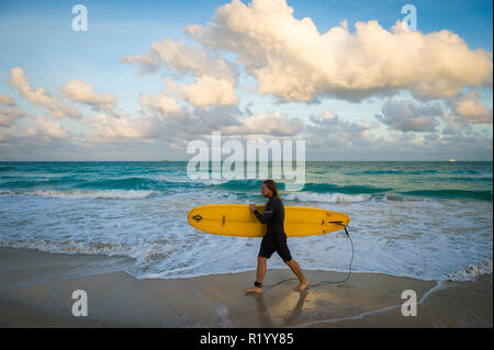 MIAMI - CIRCA SEPTEMBER, 2018: A young surfer walks carrying his longboard on the shore of South Beach. Stock Photo