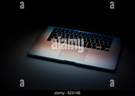Half closed silver aluminium laptop with screen light isolated on dark background Stock Photo