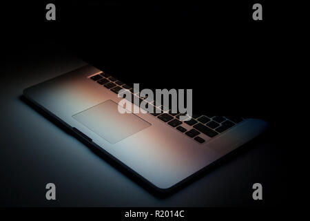 Half closed silver aluminium laptop with screen light isolated on dark background Stock Photo