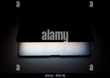 Half closed silver aluminium laptop with screen light isolated on dark background Stock Photo