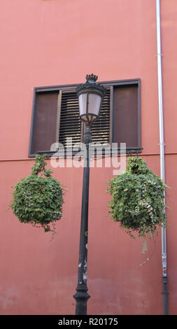 Two hanging baskets on outdoor lantern against orange red painted wall in Andalusia Stock Photo