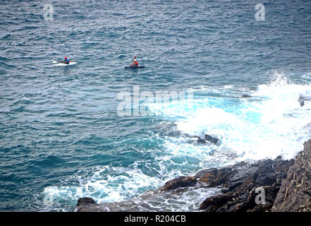 two people in kayak paddle on the stormy sea with breaking waves along the rocky coast Stock Photo