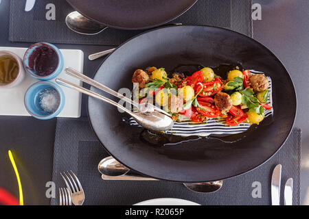 Salad with tomatoes and meat balls on a large black plate Stock Photo