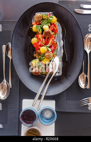 Salad with tomatoes and meat balls on a large black plate Stock Photo