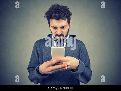 Young bearded man holding smartphone being upset with text message Stock Photo