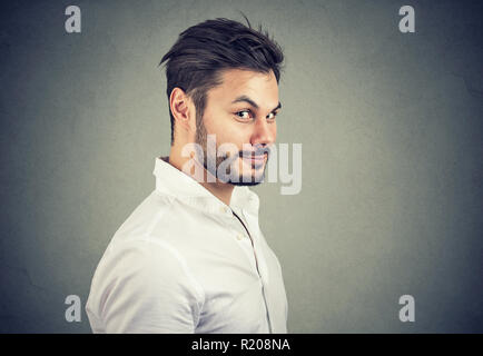 Young dishonest man in white shirt looking with pretend smile at camera on gray background Stock Photo