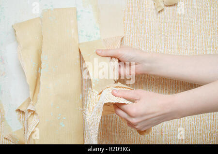 Hands of the girl. Removes the wallpaper from the wall. Close-up. Stock Photo