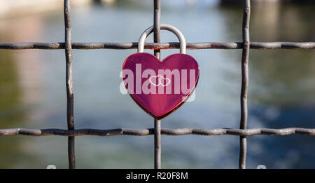 Lock your love for ever. Pink heart shaped padlock on a link fence against blurry river background. Stock Photo