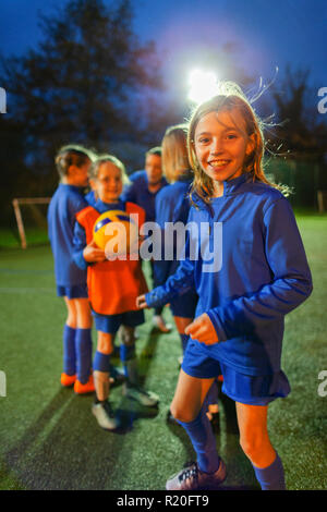 Portrait smiling, confident girl soccer player practicing with team on field at night Stock Photo