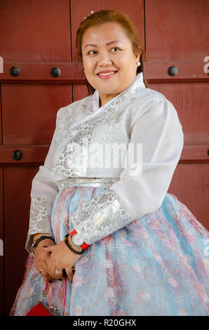 Lady tourist dressed up in traditional Korean dress, a hanbok, stood posing and smiling. Stock Photo