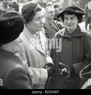 1950s, three ladies dressed in coats and hats standing together outside at a wedding, England, UK. Stock Photo
