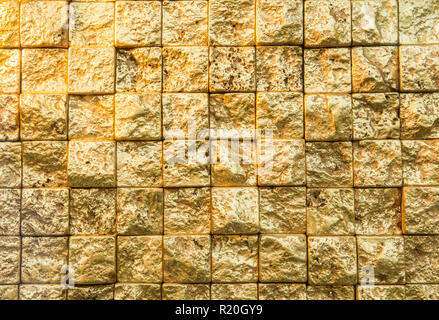Bumpy golden small even squares brick wall background. Stock Photo