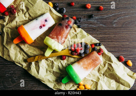 Flat lay view of lot of home made fridge frozen smoothie yogurt juice ice creams with wild berries on dark dramatic wooden background. Healthy snack c Stock Photo