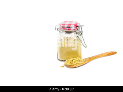 Side view of powdered mustard seeds, yellow mustard powder in cute vintage glass jar with wood spoon with pile, isolated on white background, copy spa Stock Photo