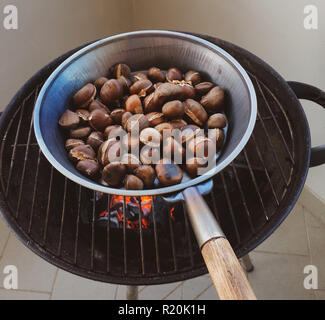 Roasted chestnuts in an iron pan cooked on the grill. Stock Photo