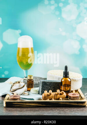 Composition wooden tray with group of different spa essentials, beard oil, gray clay soap, natural sponge, candles burning, aroma oil glass of beer on Stock Photo