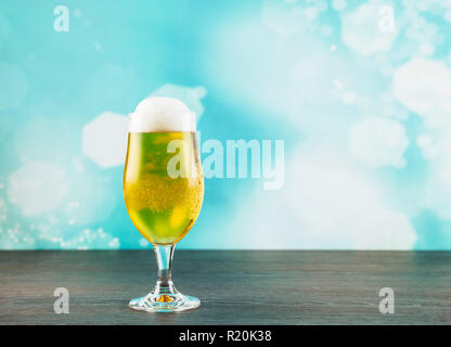 Goblet style beer glass on dark natural wooden table with light blue bokeh background. Stock Photo