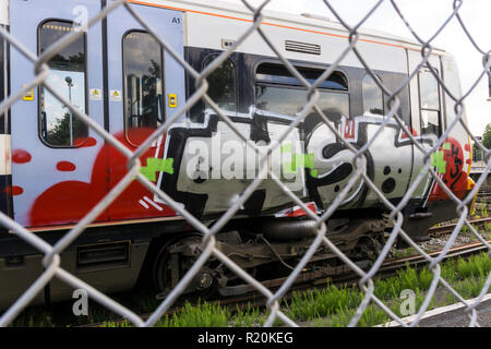 Train covered in graffiti seen through chain link fence. Stock Photo