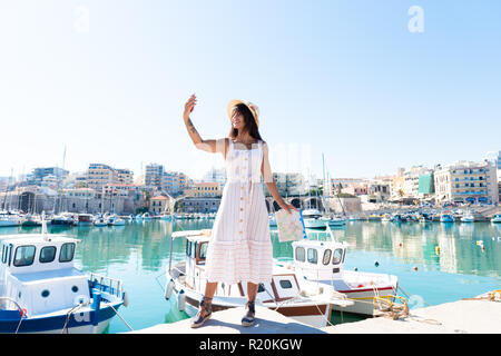 Traveling tourist woman on vacation in Heraklion Crete taking selfies at the port. Lovely elegant girl takes selfies visiting the famous Mediterranean Stock Photo