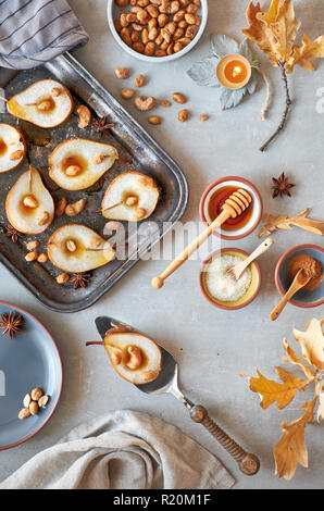 Flat lay with a tray of baked pears with caramelized nuts on gray concrete background with Autumn leaves, sugar and caramel syrup Stock Photo