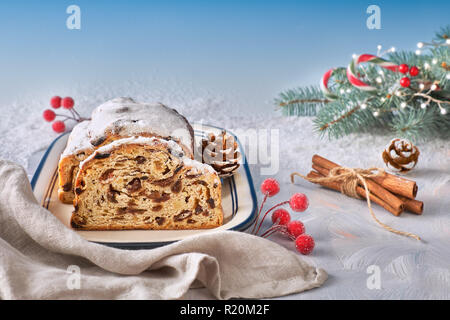 Christmas stollen on white-blue festive background with fir twigs, cones and berries. Traditional German dessert for Christmas celebration. Stock Photo