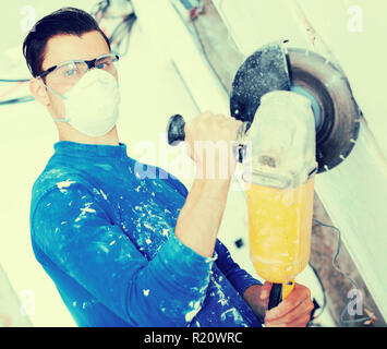 Contractor in mask using professional angle grinder for cutting wall Stock Photo