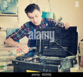 Serious adult worker repairing room and looking for necessary tool in toolbox Stock Photo