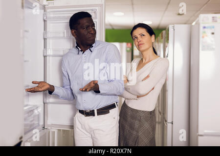 Interracial couple choosing modern fridge in store of household appliances Stock Photo