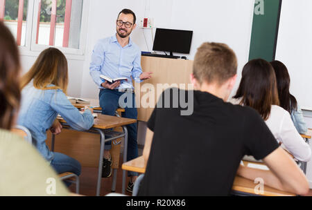 Man teacher with book is giving interesting lecture for students in the classroom Stock Photo