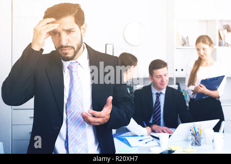 Business team tensely solving problems in office with upset man foreground Stock Photo