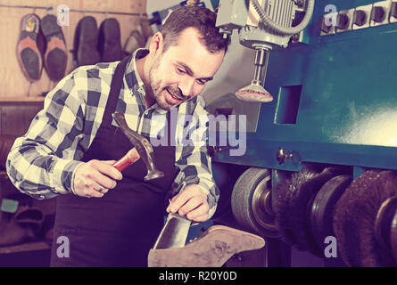 positive english male worker fixing failed shoes in shoe repair workshop Stock Photo