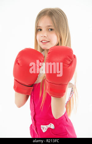 Little fighter before combat. Girl with long blond hair wearing huge red boxing gloves, sport concept. Kid in pink overalls isolated on white background. Brave girl ready to protect herself. Stock Photo