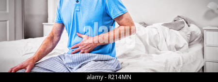Senior man having stomach pain while sitting on bed Stock Photo