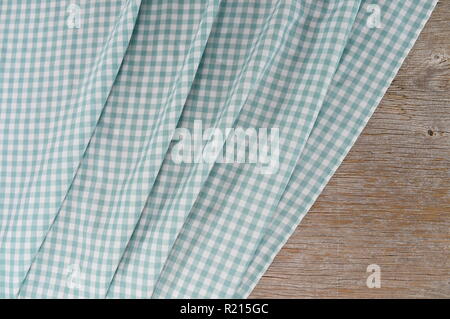 Mint and white is the checkered pattern on a tablecloth. The fabric lies in folds on old weathered wood. Stock Photo