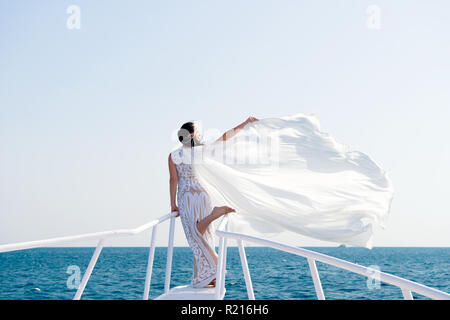 Honeymoon sea cruise. Things consider for wedding abroad. Wedding ceremony sea cruise. Bride adorable white wedding dress sunny day posing on boat or ship. Advice and tips from wedding abroad experts. Stock Photo