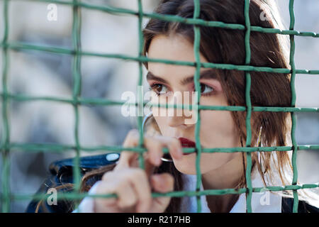 Serious fashionable photo model posing near the fence at the stadium Stock Photo