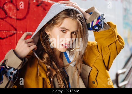 Dark-eyed young photo model wearing silver accessories posing near wall Stock Photo