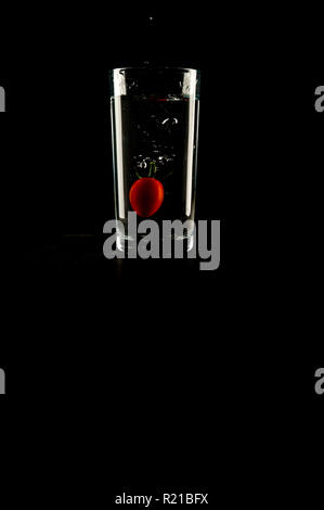 A Baby tomato splashing in to a glass of water on a black background Stock Photo