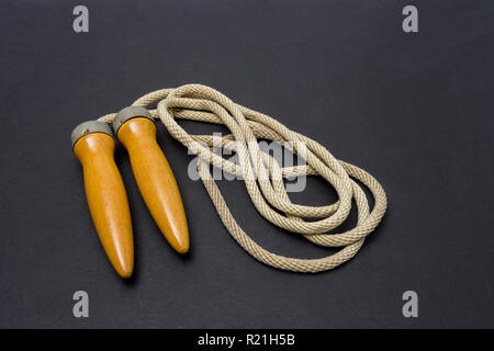 Old wooden-handled jump rope on a dark gray background. Stock Photo