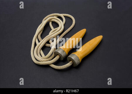 Old wooden-handled jump rope on a dark gray background. Stock Photo